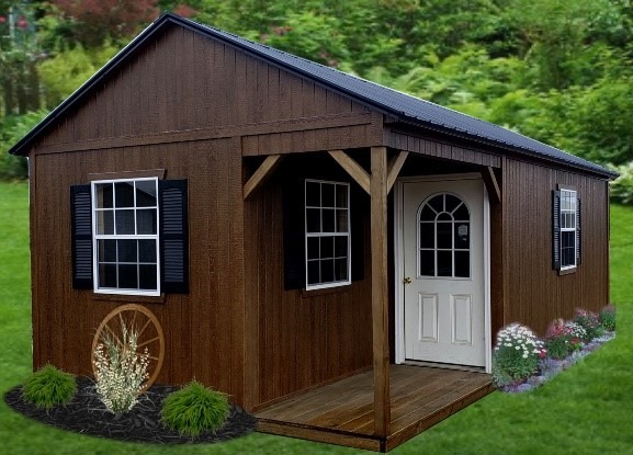 A wooden shed with a pitched roof sits on a grassy lawn. It features a white door, paned windows with black shutters, and is surrounded by small flowers and shrubs.
